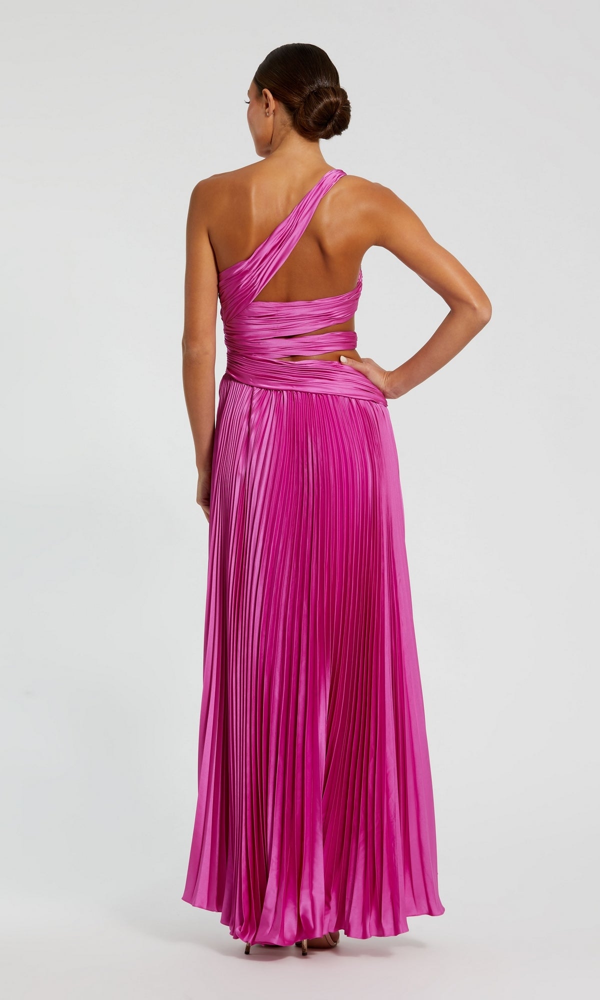 A woman faces away from the camera in a vibrant pink Mac Duggal 49837 High-Low Pleated Formal Dress, featuring elegant one-shoulder wrap detailing.